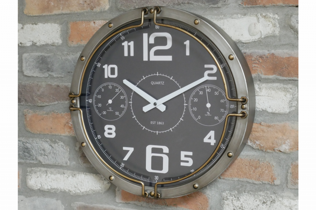 Horloge murale ronde avec un décor riveté. Cette horloge est en métal et le cadran est vitré. La finition vieillie, le décor riveté et la fixation de tubes donnent l'aspect d'un instrument de mesure. 